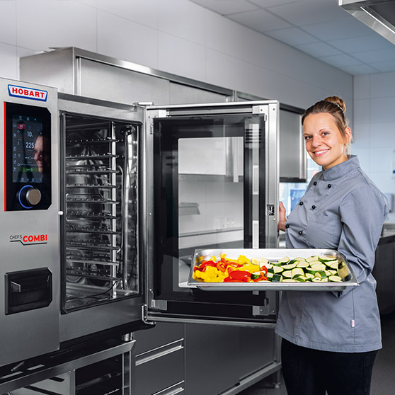Combi steamer HOBART in cucina professionale in acciaio inox, porta aperta, vassoio con verdure fresche come peperoni e zucchine per una cottura efficiente nel settore ristorazione