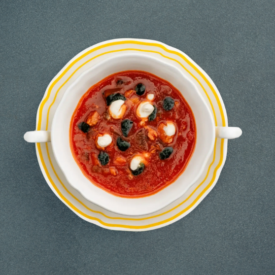 Ciotola bianca con Solyanka, zuppa tipica dell’Europa orientale a base di pomodoro, guarnita con panna acida e olive nere, servita su piatto a righe gialle