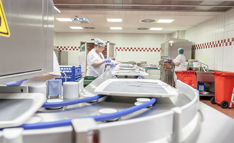 Moderna area di lavaggio con HOBART FLOW Line autoLINE, sistema di lavaggio automatico con nastro trasportatore e postazioni di lavoro per pulizia efficiente di vassoi, piatti e bicchieri, costruzione in acciaio inox per flussi igienici e ottimizzati.