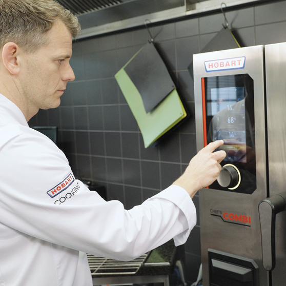 Cuoco che utilizza il pannello touch del HOBART CHEF’S COMBI in una cucina professionale, regolando i parametri per una cottura precisa ed efficiente.