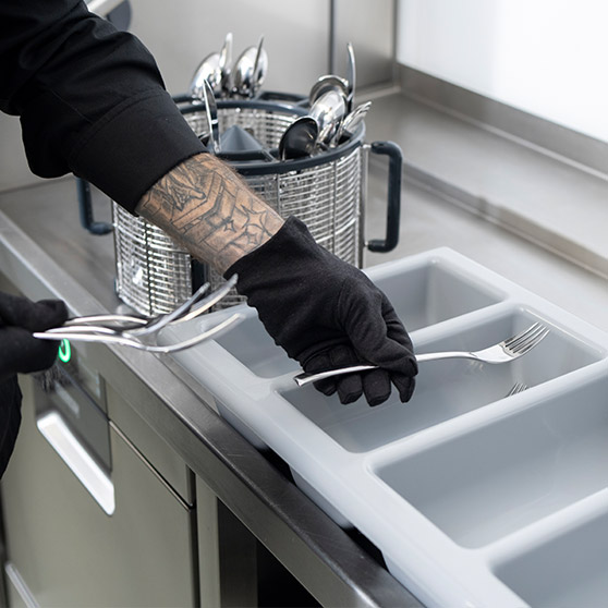 Primo piano di un operatore che ordina posate appena lavate accanto a una lavastoviglie sottobanco HOBART con funzione BESTECK PREMIUM.
