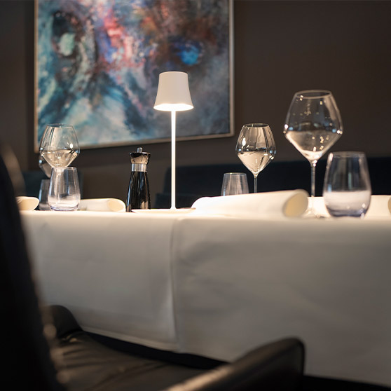 Primo piano di una tavola apparecchiata in stile fine‑dining al ristorante RIVA con calici eleganti, tovagliato bianco e illuminazione moderna.